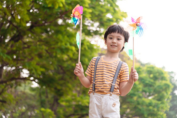 Boy playing with windmill, running, jumping in the park on summer vacation concept for freedom or the environment