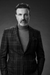 Obraz premium Portrait of a stylish elegant senior businessman with a beard and casual business clothes in photo studio isolated on dark background gesturing with hands