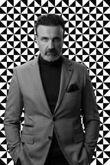 Black and white portrait of a stylish elegant senior businessman with a beard and casual business clothes against retro colorful pattern design background gesturing with hands