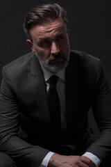 Obraz premium Portrait of adult businessman wearing trendy suit and sitting in modern studio on stylish chair against the black background