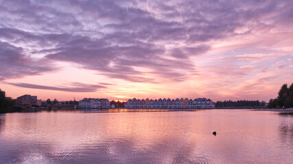 Purple skies and sunset over lake De Rietplas in Houten in the Netherlands. Row of colourful wooden newly built Dutch houses in the distance.