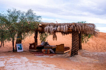 Sofa with cushions under shelter on sand dunes in sahara desert on summer day, Hut on sand in desert