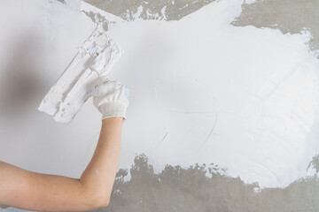 Caucasian female worker putty with a spatula with putty concrete walls in the house