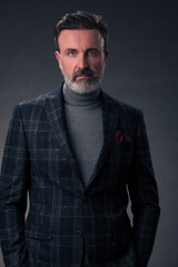 Portrait of a stylish elegant senior businessman with a beard and casual business clothes in photo studio isolated on dark background gesturing with hands