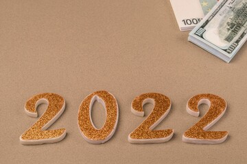 Golden numbers 2022 and bundles with money in dollars and euros on a beige background. Copy space