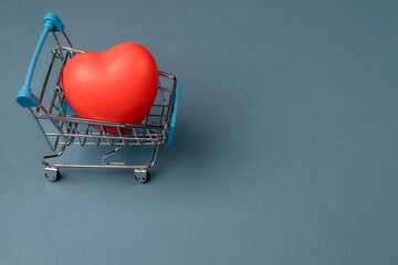 Rubber red heart in a shopping trolley on a blue background. Copy space
