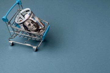 One hundred dollar bills in a shopping trolley on a blue background. Copy space