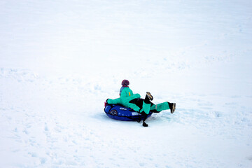 Fototapeta na wymiar Child having fun on snow tube. Kid is riding a tubing, winter entertainment