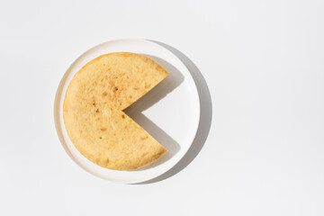 Tortilla de patatas española hecha con aceite de oliva, huevos y patatas en un plato blanco sobre una mesa blanca. Aperitivo español. Vista superior	