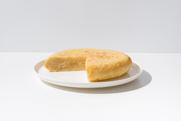 Tortilla de patatas española hecha con aceite de oliva, huevos y patatas en un plato blanco sobre una mesa blanca. Aperitivo español	