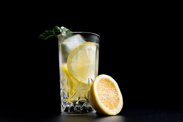 Un vaso de refrescante limonada, cóctel de frutas con rodajas de limón y hielo sobre fondo negro
