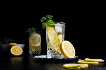 Dos vasos de refrescante limonada, cóctel de frutas con rodajas de limón y hielo sobre fondo negro