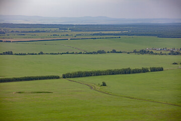 Obraz premium The view from the mountain to agricultural fields, separated by forest belts. Mountains on the horizon, summer cloudy landscape.