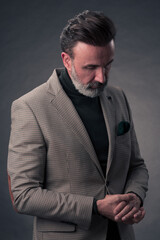 Portrait of a stylish elegant senior businessman with a beard and casual business clothes in photo studio isolated on dark background gesturing with hands