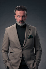 Obraz premium Portrait of a stylish elegant senior businessman with a beard and casual business clothes in photo studio isolated on dark background gesturing with hands