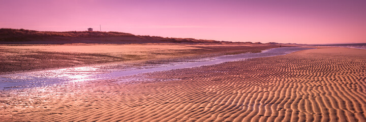 Pink sunset over the coastal horizon. Tropical seascape with the view of undulating rippled sand...