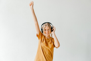 Happy young woman in white headphones enjoys listening to music on white background