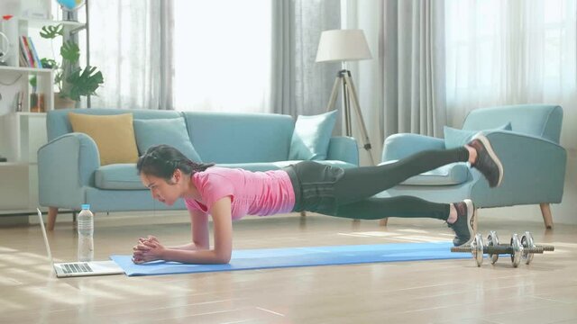 Asian Woman Doing Yoga Plank And Watching Online Tutorials On Laptop, Training In Living Room
