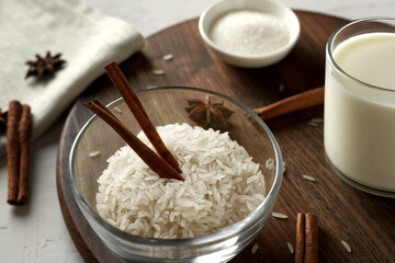 Glass bowl with rice grits and cinnamon sticks. Ingredients for rice milk porridge - rice, milk,...