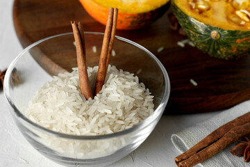 Glass bowl with rice grits and cinnamon sticks. Ingredients for making pumpkin porridge with rice. Selective focusing.