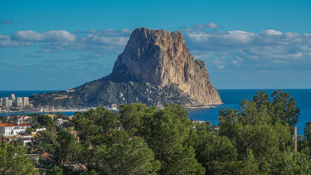 Pe&ntilde;&oacute;n de Ifach desde Morro de Toix entre pinos viendo su cara oeste junto al puerto deportivo y pesquero