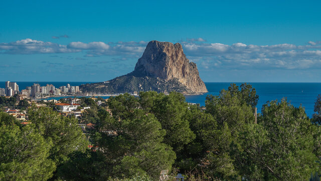 Pe&ntilde;&oacute;n de Ifach desde Morro de Toix entre pinos viendo su cara oeste junto al puerto deportivo y pesquero