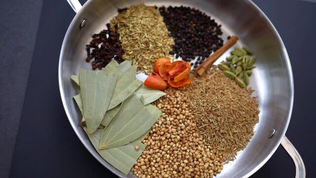 Slow motion footage moves over a pan filled with Indian curry spices. Food herbs and spices arranged in a metal pan against a plain dark background with copy space available. Food footage 