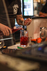 bartender preparing a red cocktail with ice and red berries in a glass inside a bar