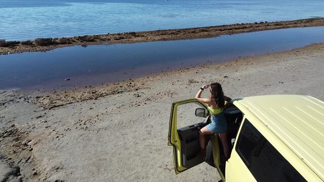 yellow camper van arrives at the beach in front of the sea during a summer trip - girl alone traveling goes down and looks at the sea - view from the drone in Murcia Spain Mar minor 