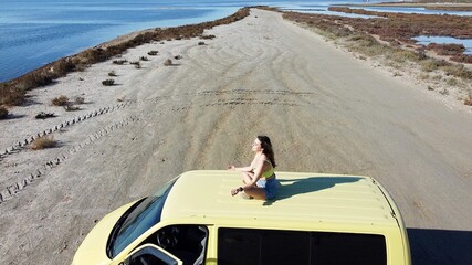Girl traveler lives the adventure in freedom with yellow vintage camper sitting on the roof of the van relaxes and enjoys nature at the beach in front of the sea in Murcia Spain - Joga meditation 