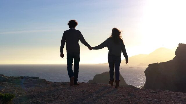 man and woman walk on a cliff by the sea at sunset in total freedom of nature - they spread their arms holding hands, kiss and hug during the journey in Murcia Spain La Manga