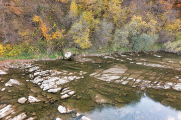 River stream running past mountain foot with autumn forest