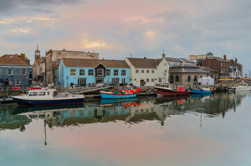 Fototapeta na wymiar Dusk / Sunset at Weymouth Harbour / Harbor showing fishing boats, pubs and restaurants.