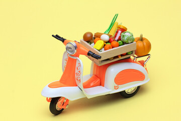 An orange toy scooter delivering products: fresh fruits and vegetables in a wooden box