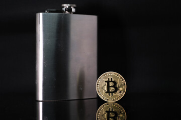  bitcoin coin stands next to a steel hip flask