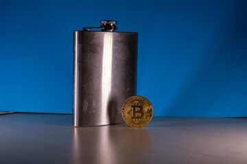  bitcoin coin stands next to a steel hip flask