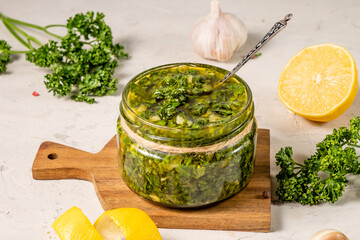 Green chimichurri sauce on a background of parsley, lemon, white table.