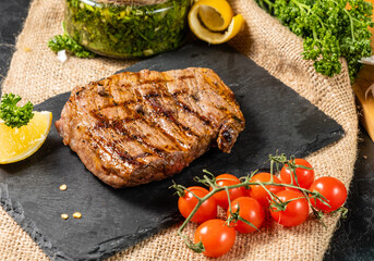 Beef steak on a black stone tray with cherry tomatoes, lemon on the background.