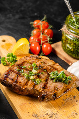 Beef steak on a wooden board, against a background of cherry tomatoes, lemon.