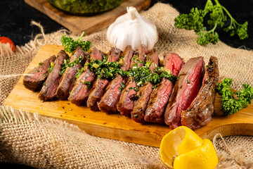Steak, cut into pieces of medium fried, poured with chimichurri sauce, served on a wooden board.