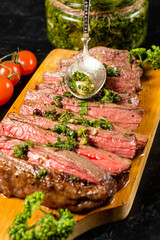 Medium-rare cooked juicy beef cuts are spooned with homemade chimichurri sauce.