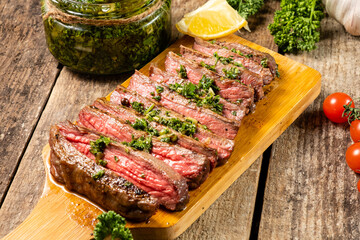 Juicy steak with chimichurri sauce served on a wooden board. Old wooden table.