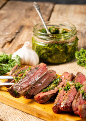 Juicy grilled meat, beef steak chopped on a wooden board and a fork with a piece of meat and chimichurri sauce.