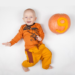 Smiling happy newborn infant nine month baby in the orange clothes on bed bright airy copy space childhood with pumpkin with the number 9 carved on it to indicate age