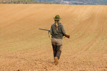 Hunter woman with shotgun hunting in the field.