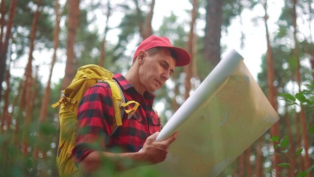 tourist hiker with a navigation map looking for a path in the forest park. travel trekking concept. adventure in the forest park. hiker with a map lifestyle in his hands search navigation