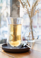 Glass cup with green or herbal tea on wooden table in cafe. Blurred window background.