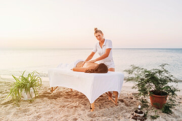 Girl masseur at work on background of seascape. Beach massage at resort. Portrait of masseur doing...