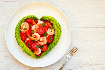 Heart shaped avocado with roasted shrimps,cherry tomatoes and parleys on plate with white wood background.Love healthy food concept for Valentine's day.Top view.Copy space