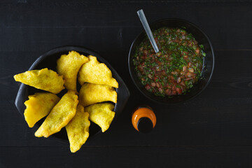 Colombian Empanadas with spicy chili on black background. Hand with an empanada. Copy space. Colombian cuisine.